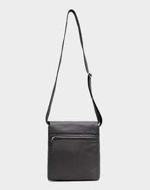 The Rudsak MADDY - 8322512 BLACK is a minimalist black leather messenger bag with an adjustable strap, front zippered pocket, and rectangular shape, shown against a plain light gray background.
