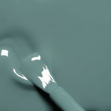 A close-up of a Manucurist Sage nail polish brush coated in glossy, muted sage green polish rests on a matching liquid surface with reflected highlights.