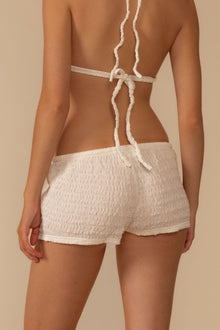 Cream textured low-rise shorts with drawstring waist tie, shown from back view on model.