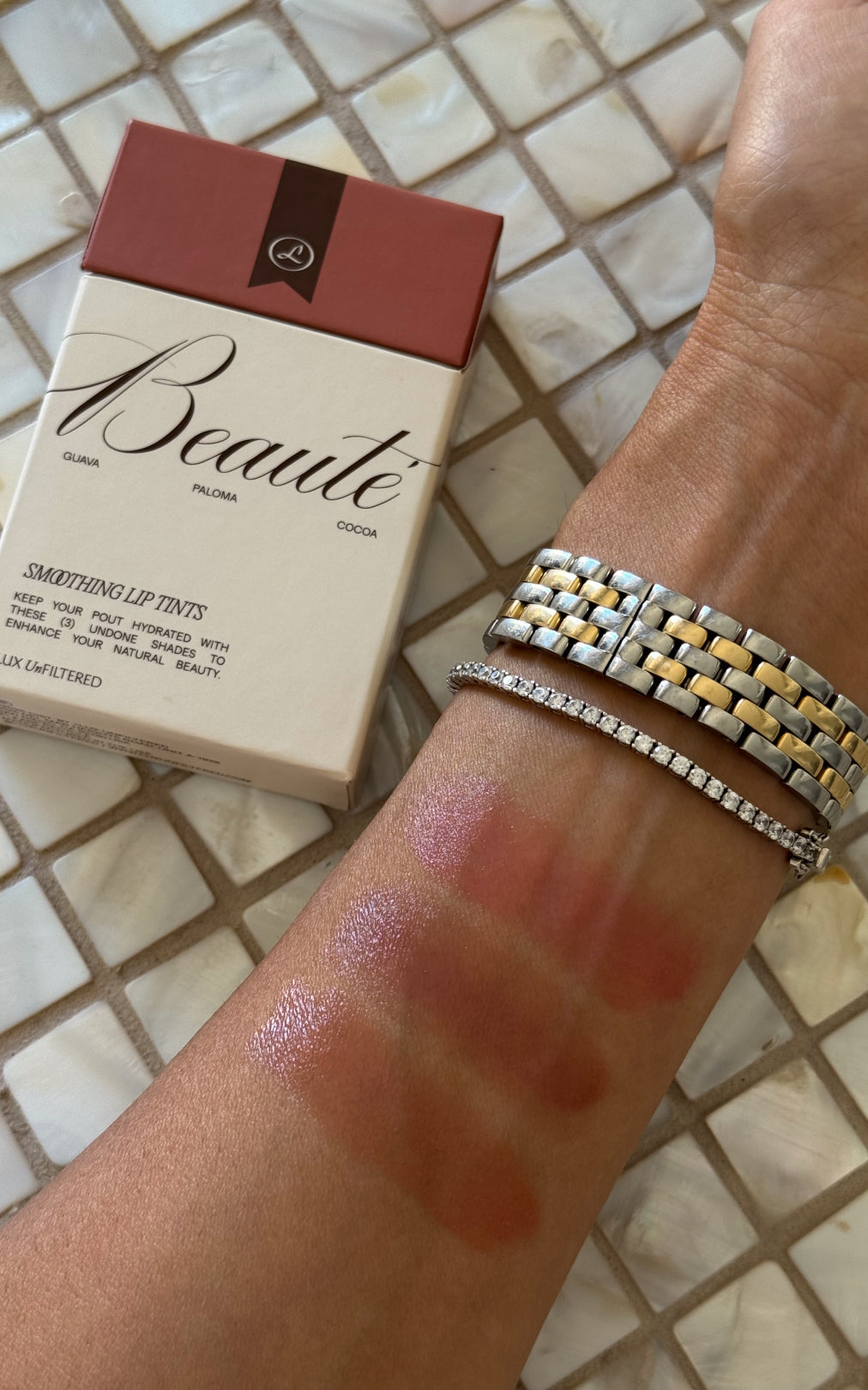Arm with four pink lip-tint swatches and bracelets beside a Beauté lip tint box labeled Beauté; shades Guava, Paloma, Cocoa.