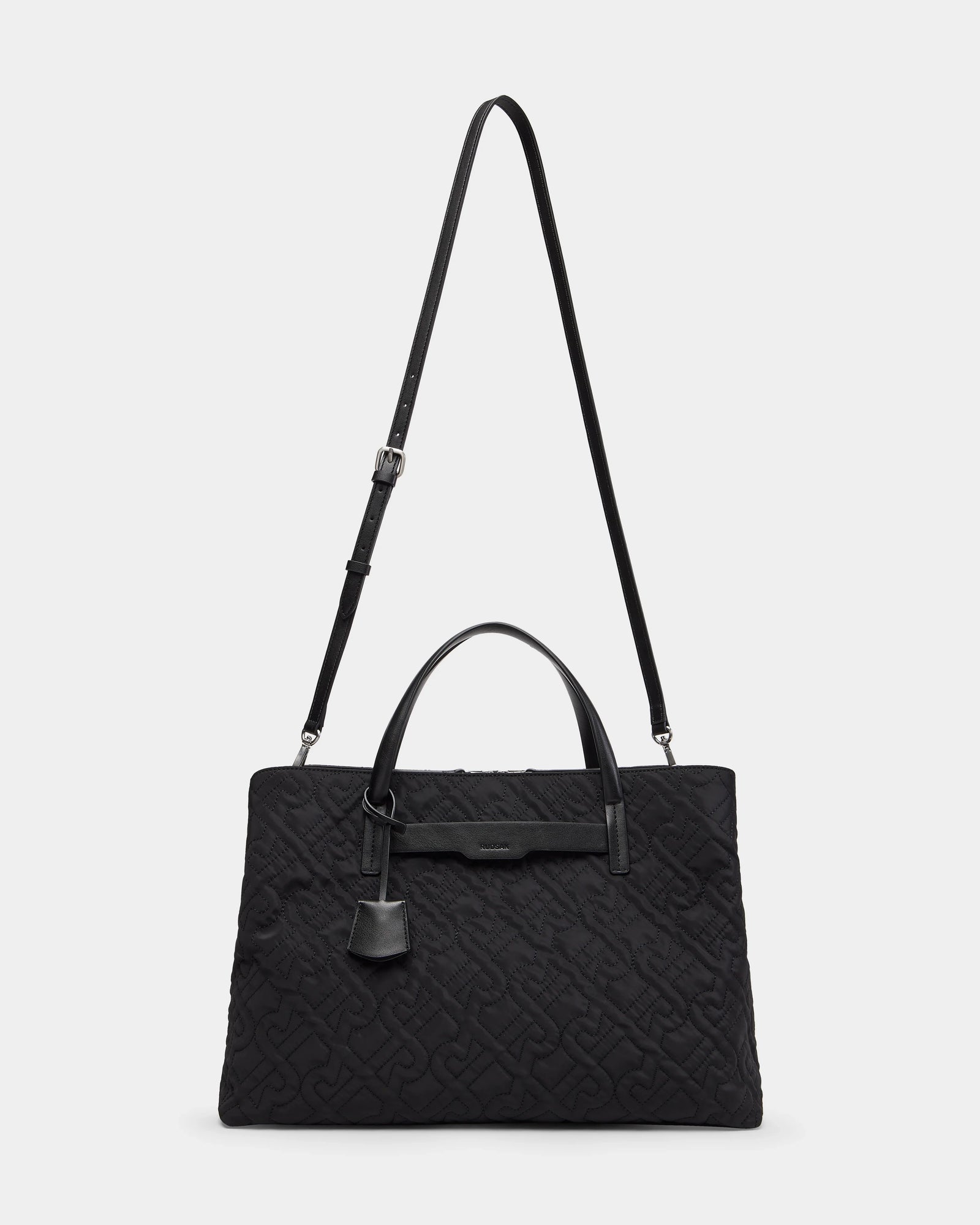 The Rudsak ASMINE - L325005 Black is a black quilted monogram tote with embossed patterns, two short handles, an adjustable shoulder strap, and a leather tag—an elegant work bag for any occasion, shown against a plain white background.