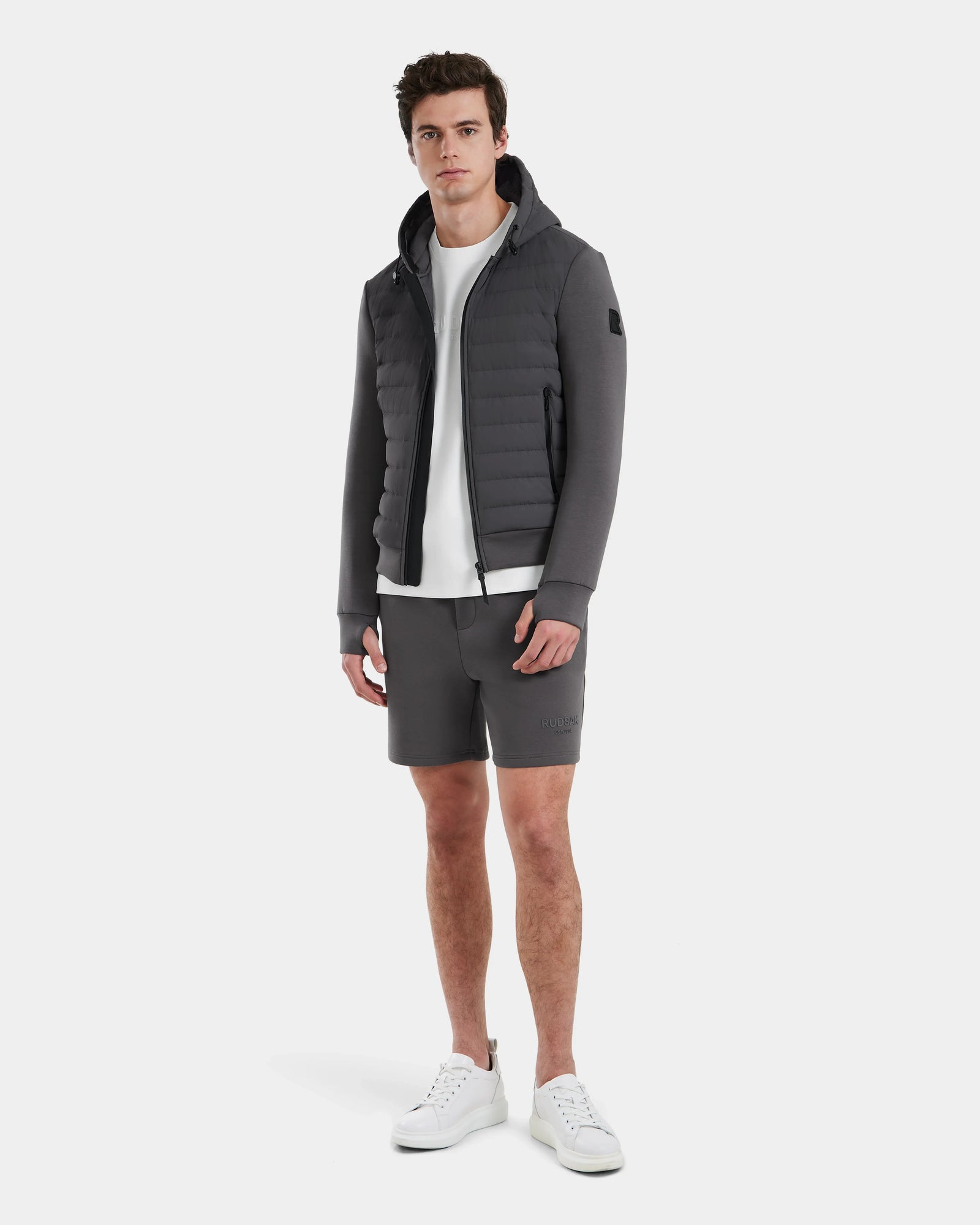 A man faces forward wearing the Rudsak DEE MAT - 6124028 Grey lightweight down jacket over a white t-shirt, gray shorts, and white sneakers against a plain white background.