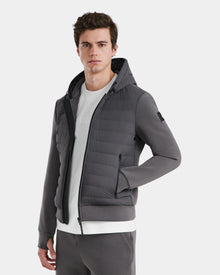 A young man showcases the Rudsak DEE MAT - 6124028 Grey men’s lightweight hybrid down jacket and matching pants, highlighting wind and water-resistant urban style essentials against a plain light background.