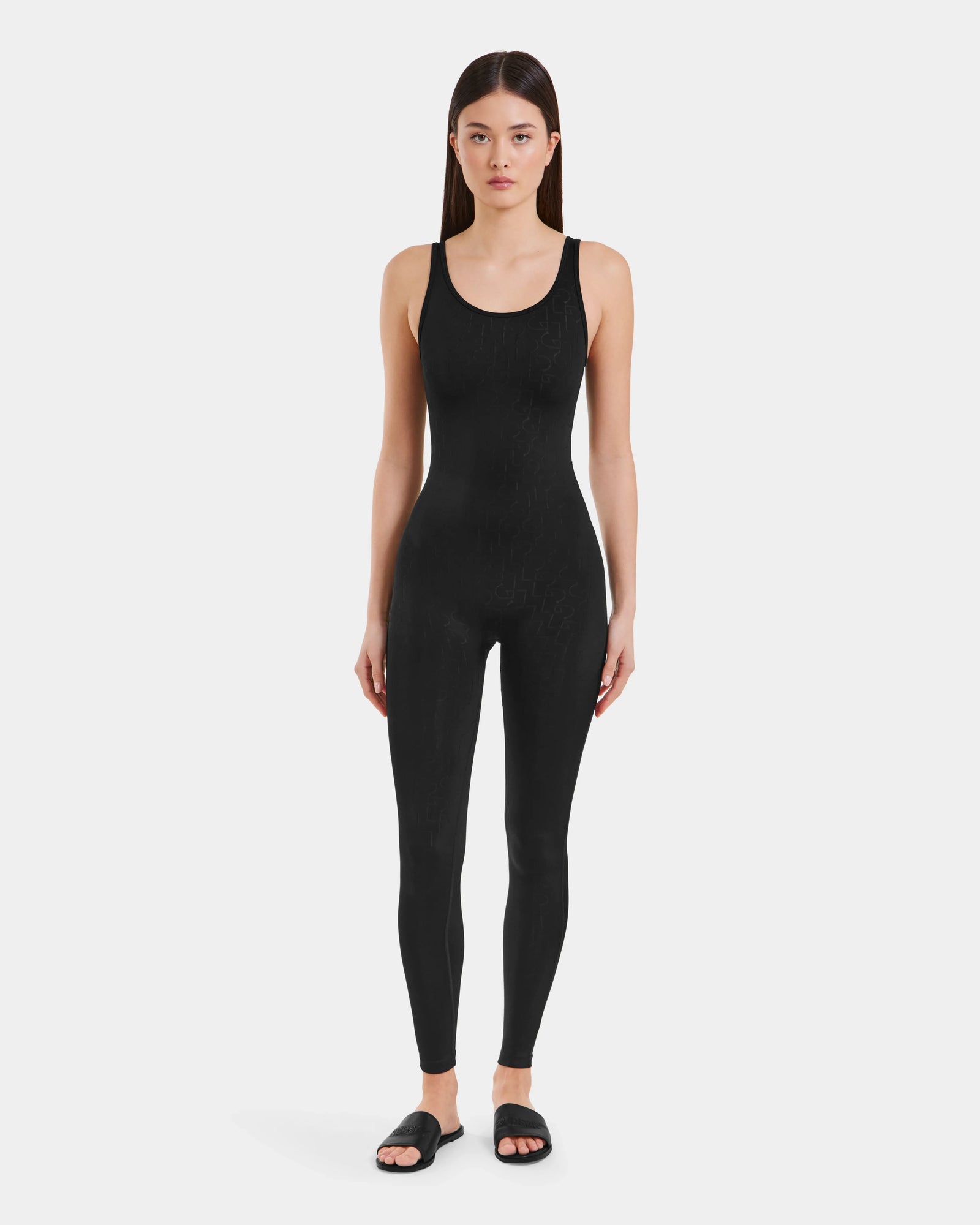 A woman faces forward against a light background, wearing the LAWREN - 8523054 Rudsak Pattern black monogram bodysuit and black slide sandals by Rudsak.