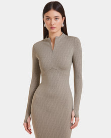 A woman with long straight hair models the Rudsak MAYLIN - 8523504 Cement Pattern dress, a women’s taupe fitted dress in stretch fabric with a subtle geometric design and short front zipper, standing against a plain white background.