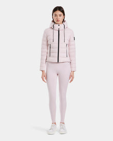 A woman faces forward, wearing the Rudsak MELISSA - 8125054 light pink puffer jacket with a hood, matching light pink leggings, and white sneakers against a plain white background.