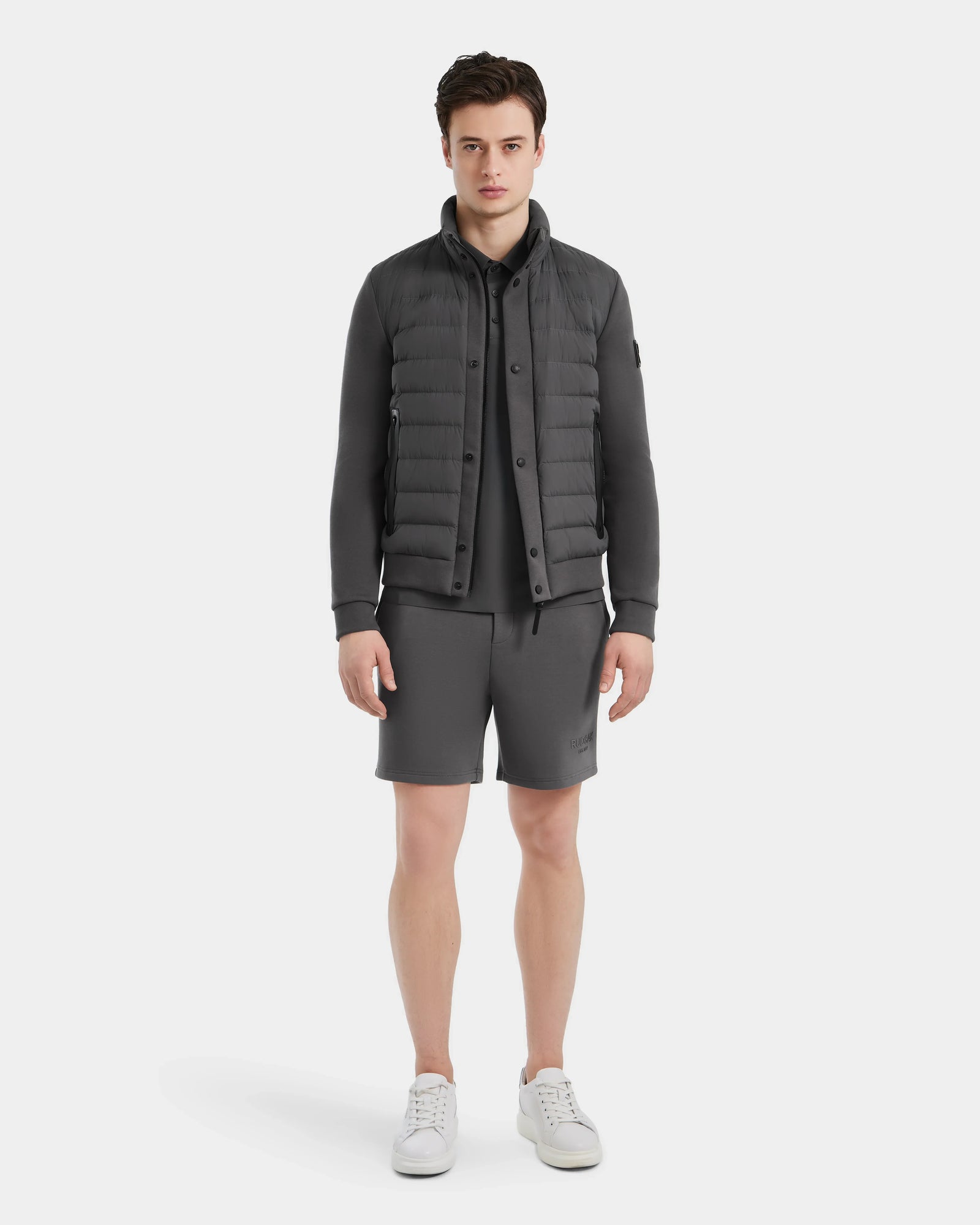 A young man faces forward, wearing the Rudsak RAGAB - 6124577 Grey men’s hybrid jacket with lightweight down insulation over a matching shirt and shorts, paired with white sneakers, against a plain white background.