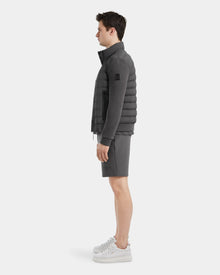 A man stands in profile against a plain background, wearing the Rudsak RAGAB - 6124577 Grey mens hybrid jacket with lightweight down insulation, matching shorts, and white sneakers—ideal for transitional weather.