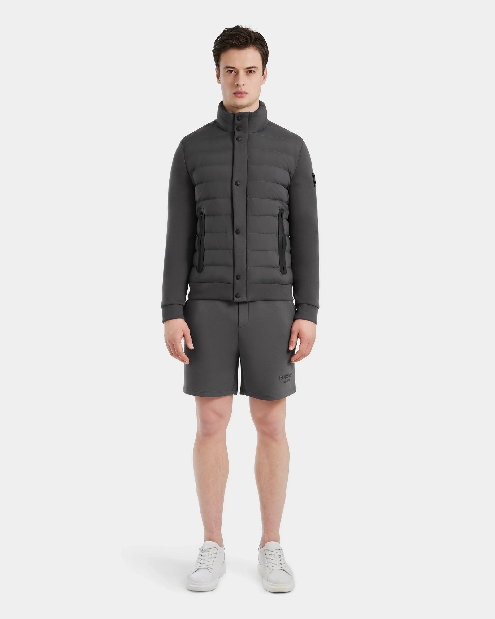 A man stands facing forward, wearing the Rudsak RAGAB - 6124577 Grey men’s hybrid jacket, paired with matching gray shorts and white sneakers, against a plain white background.