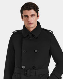 A man with short brown hair wears the Rudsak TIMOTHY - 6124589 black mens trench coat, featuring a belt and shoulder epaulets, standing against a plain white background.