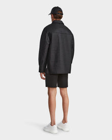 A man faces away in a Rudsak KERRY - 9124003 Black M quilted shirt jacket with eco-friendly insulation, paired with black shorts, black cap, and white sneakers against a plain white background.