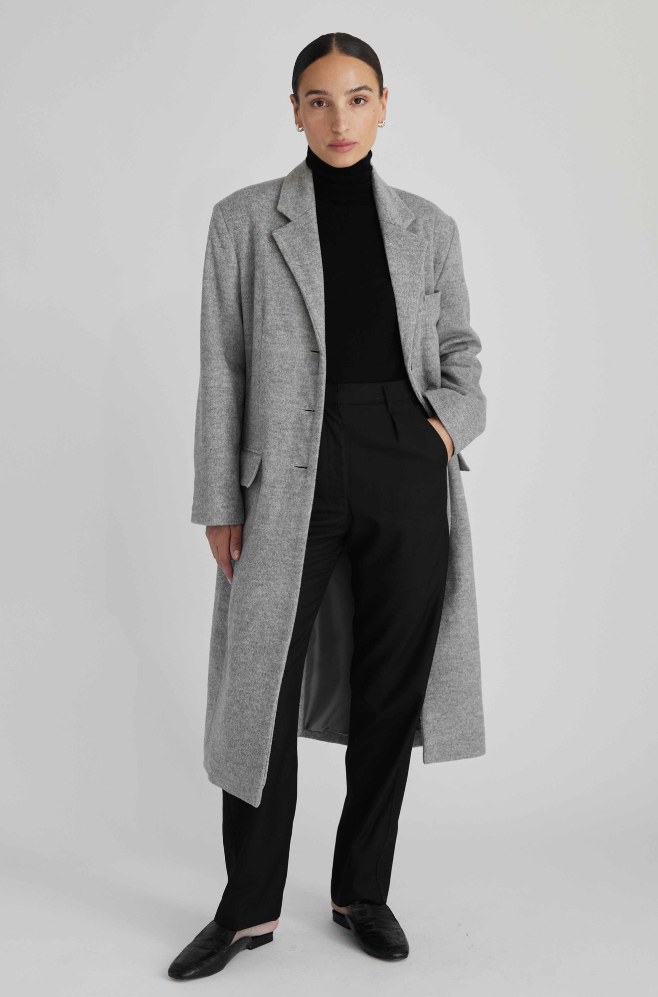 Person wearing a gray coat over a black outfit on a light gray background