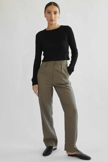 Woman wearing a black top and beige pants on a white background