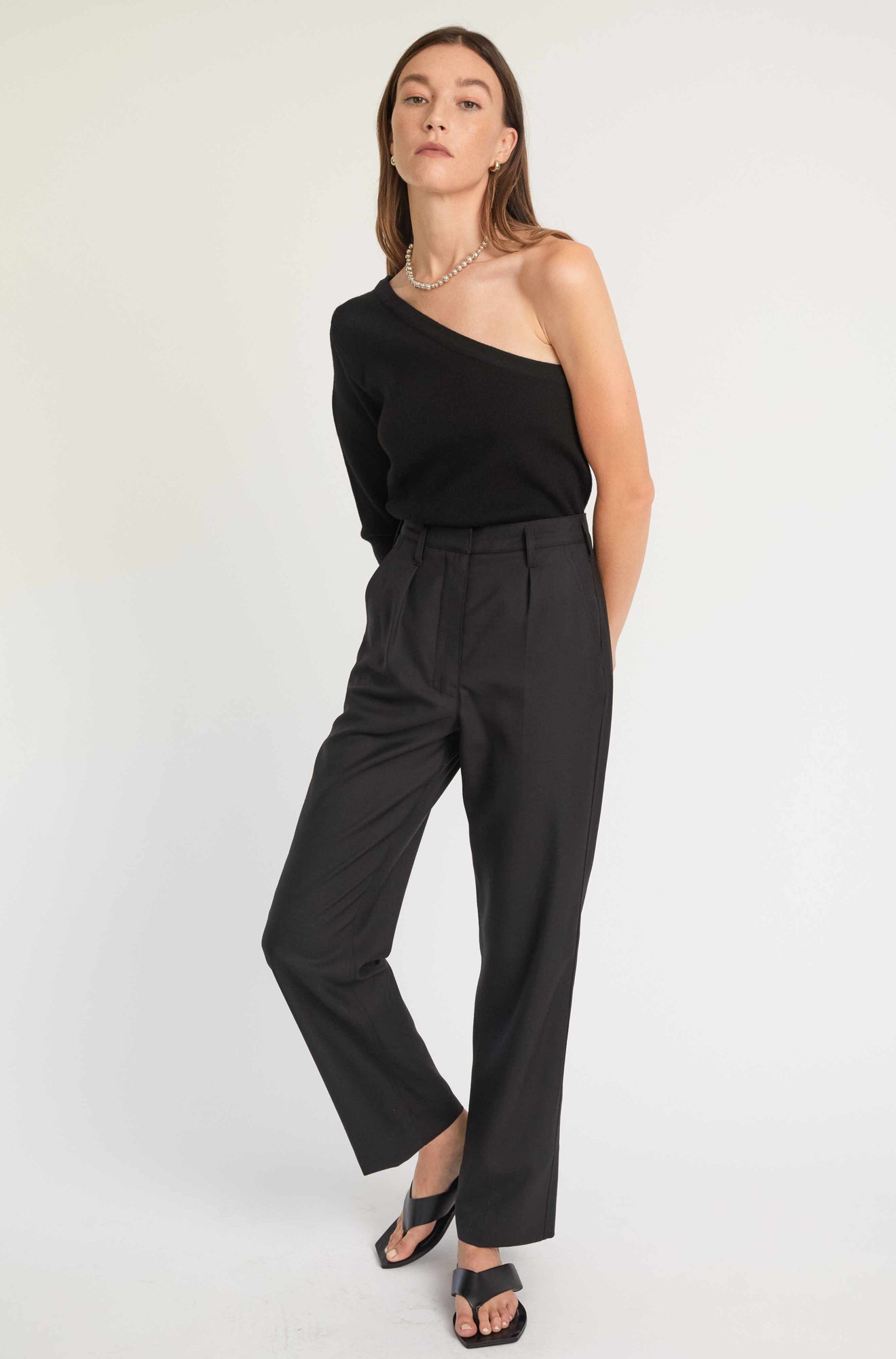 Woman wearing a black one-shoulder top and black pants on a white background