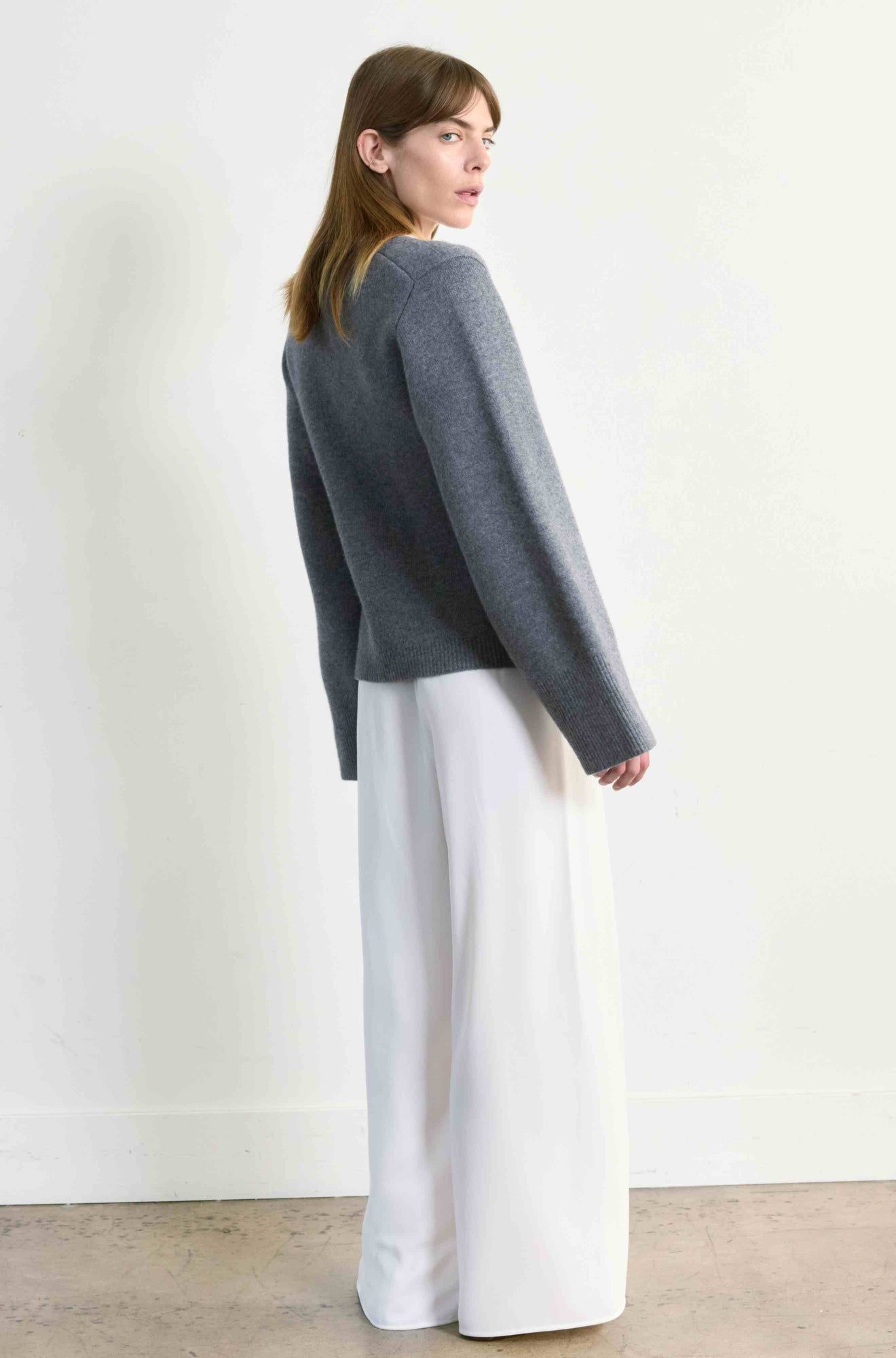 Woman wearing a gray sweater and white pants against a plain background