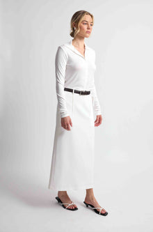 Woman wearing a white button up top with a white skirt and brown belt