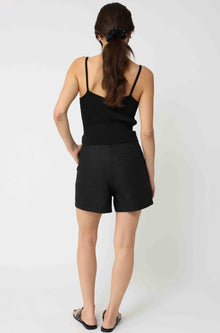 Woman wearing a black tank top and black linen shorts against a light grey background