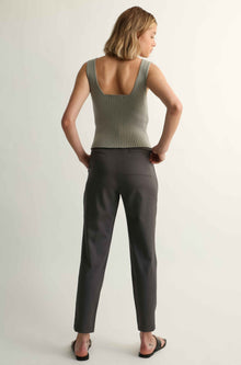 Woman wearing a green tank top and gray pants on a plain background