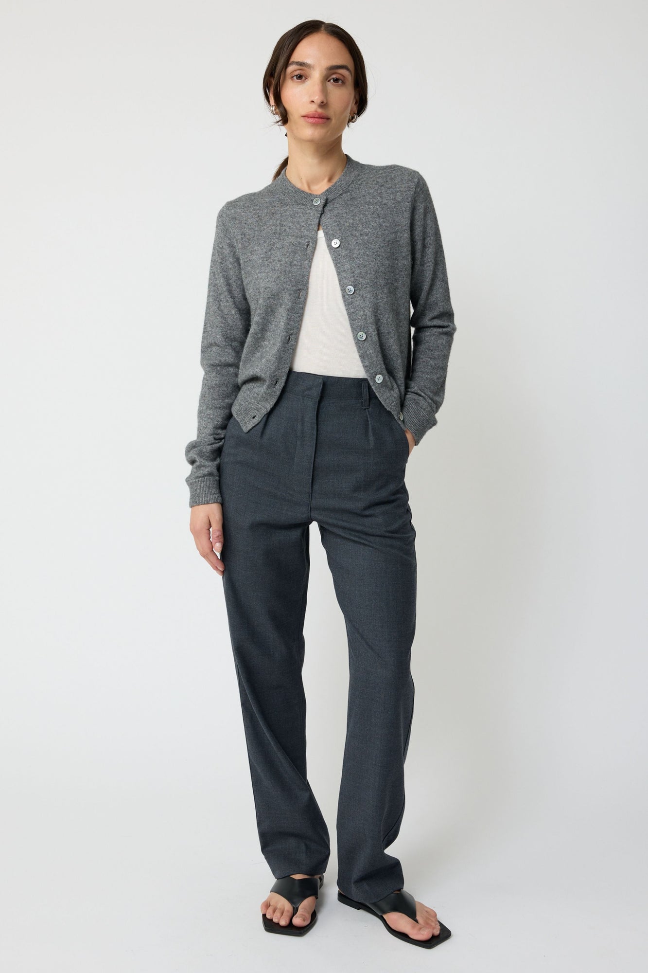 Person wearing a gray cardigan and dark pants on a white background