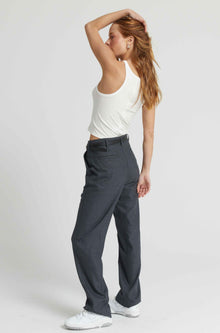 Woman wearing gray pants and a white top on a plain background