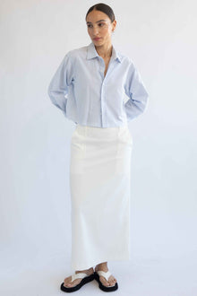 Woman wearing a light blue striped shirt and white skirt on a plain background