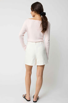Woman wearing a light pink sweater and white shorts on a plain background