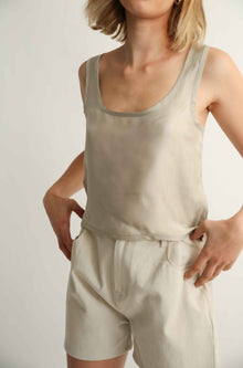 Woman wearing a silk top and beige shorts against a grey background