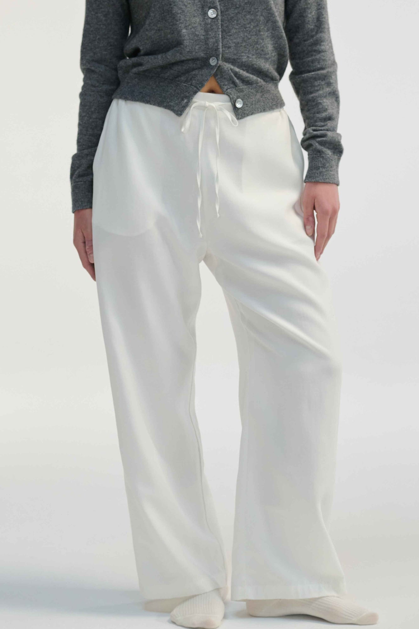 Woman wearing white linen pants on a light grey background