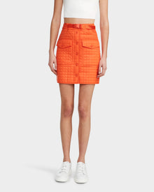 A woman models the Rudsak SABINE - 8524063 Orange Sorbet, a bold womens statement piece, featuring a quilted short skirt with flap pockets, matching belt, and a contemporary edge against a plain background.