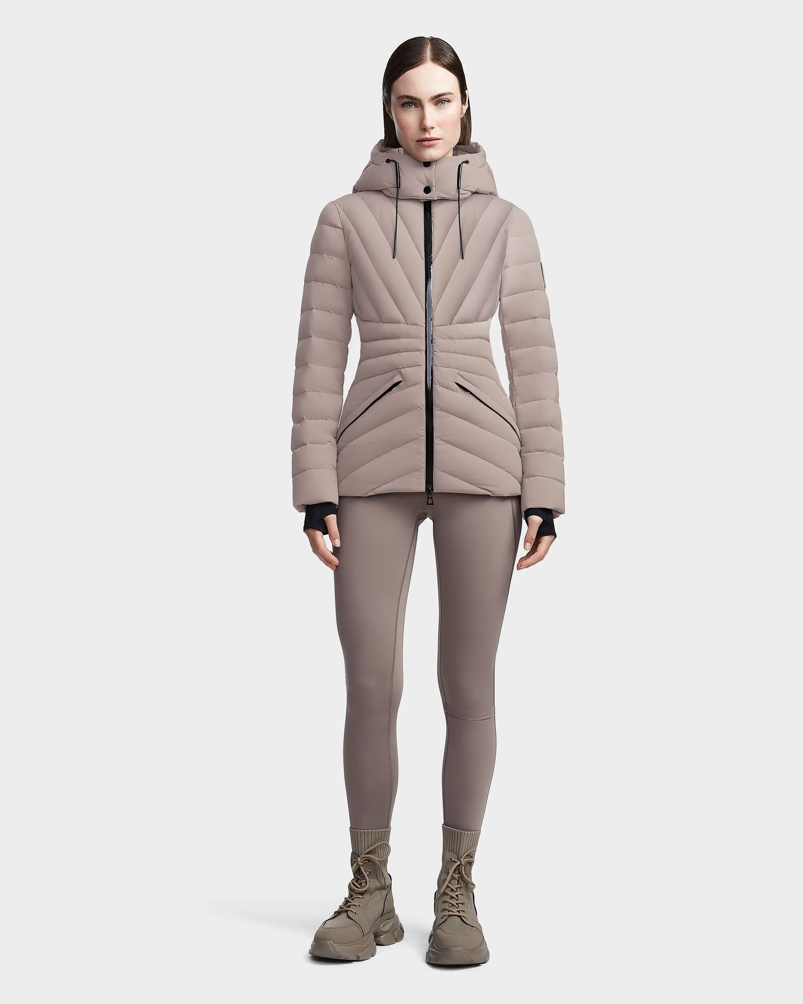 A woman faces forward against a plain light background, wearing the Rudsak HANNA - 8123562 Cement RDS certified quilted down jacket with hood, matching fitted pants, and tan lace-up boots.