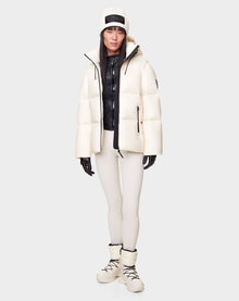 A woman faces forward wearing the RUDSAK DORA - 8122547 ICELAND white jacket with removable hood, black zip-up top, white leggings, black gloves, and white winter boots against a plain light background.