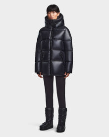 A person models the Rudsak RITA S - L123527 Black women’s down puffer jacket with matching black pants and black puffer boots against a plain light gray background.