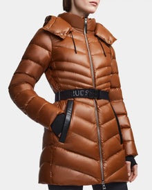 A person wearing the MALAYA - L123510 Dark Camel down puffer jacket by Rudsak, featuring herringbone quilting, a belted waist, hood, black accents, front zipper, and hands tucked into the pockets.