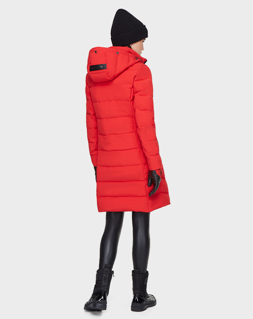 Wearing the Rudsak ELISA - L121512 POPPY RED women’s quilted down puffer with a hood, black beanie, gloves, leggings, and boots, a person stands facing away on a light background—an ideal sustainable winter jacket for cold days.