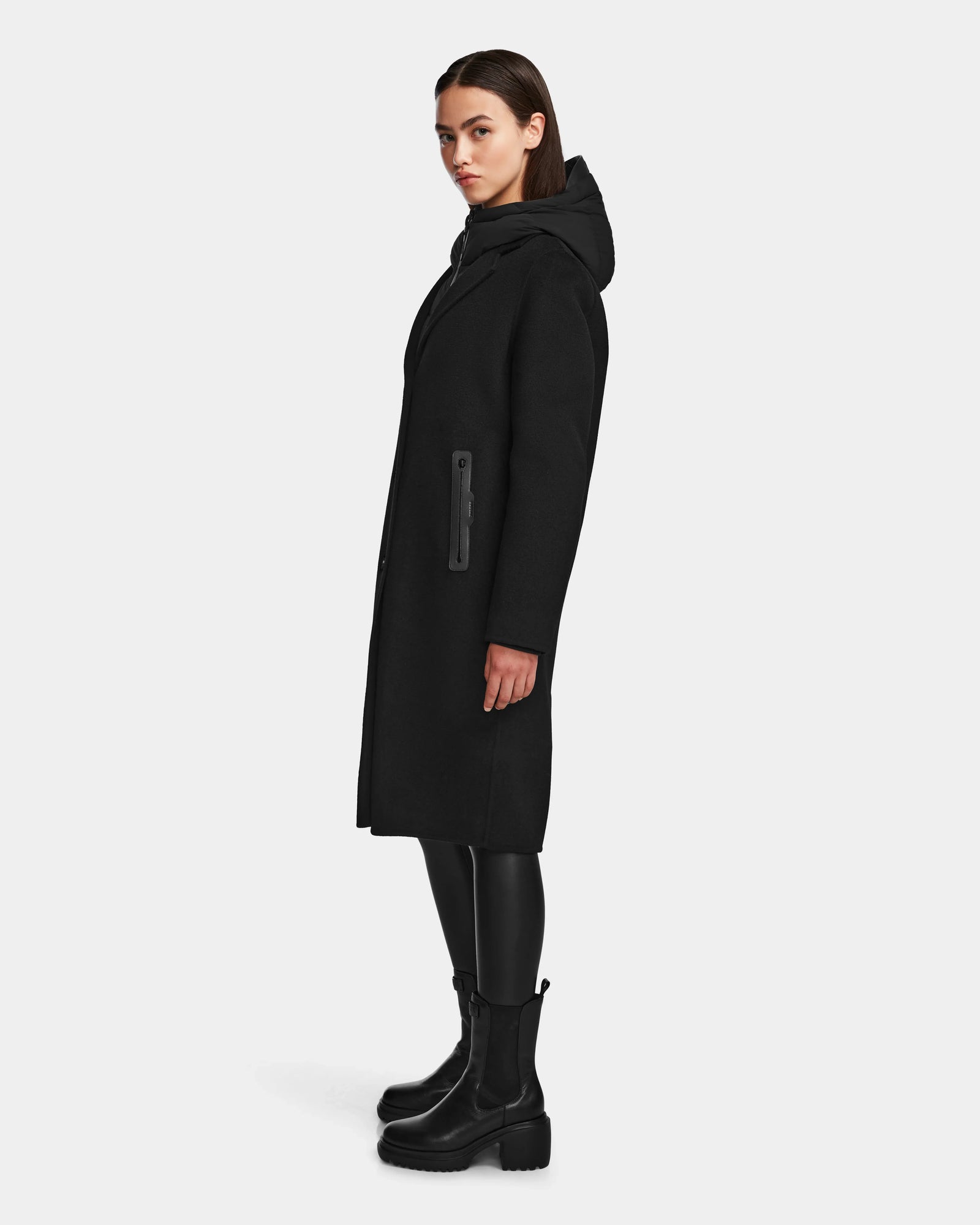 A woman stands confidently in the Rudsak ARLA - 8124579 Black coat, its classic double-breasted design elevated by sleek leather sleeves.