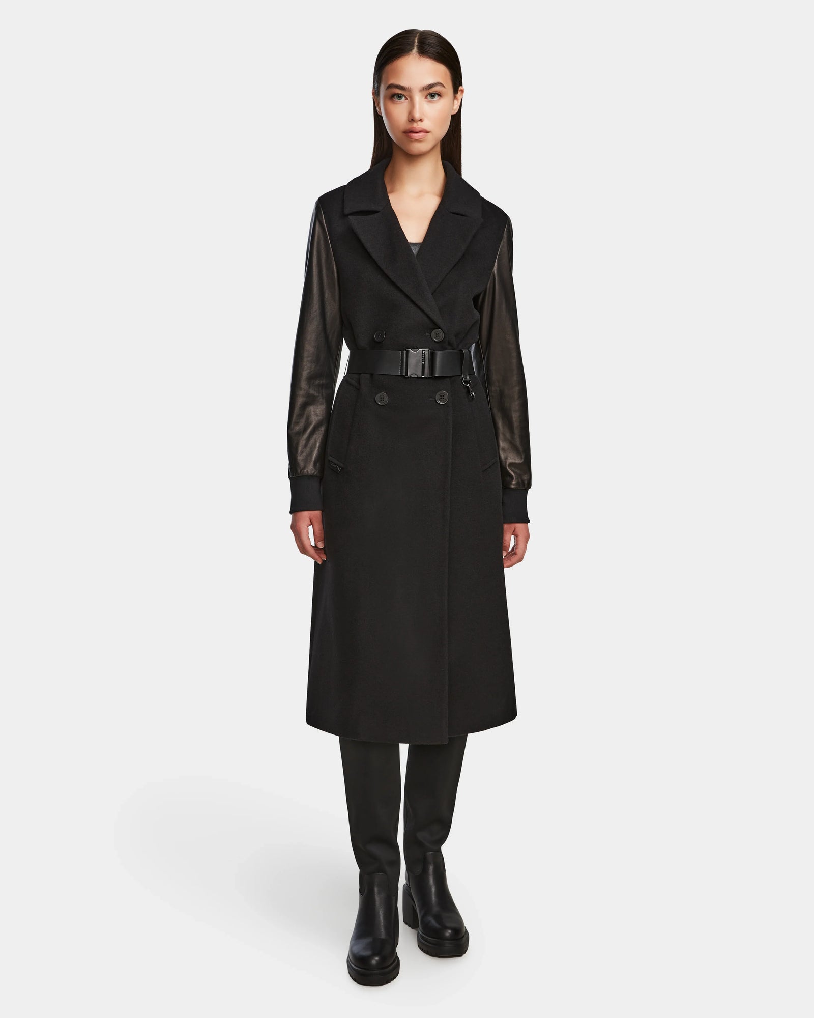 A woman faces forward in the MARYLIN - 8124520 Black by Rudsak, a long black womens wool coat with leather sleeves, worn with black pants and boots against a plain white background.
