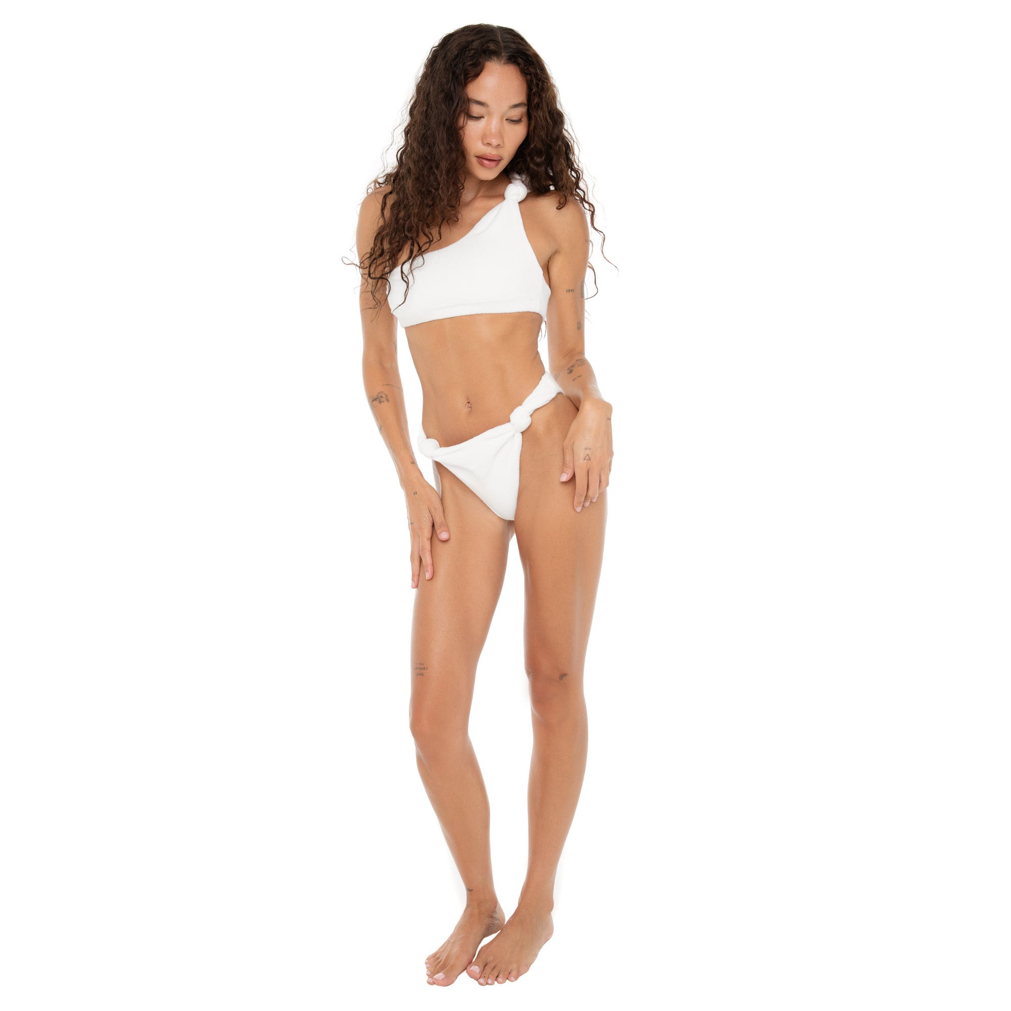 Full-body shot of model wearing the Are You Am I Aimi Bikini Top in white terry, styled with matching bottoms, featuring a one-shoulder knotted strap. **white