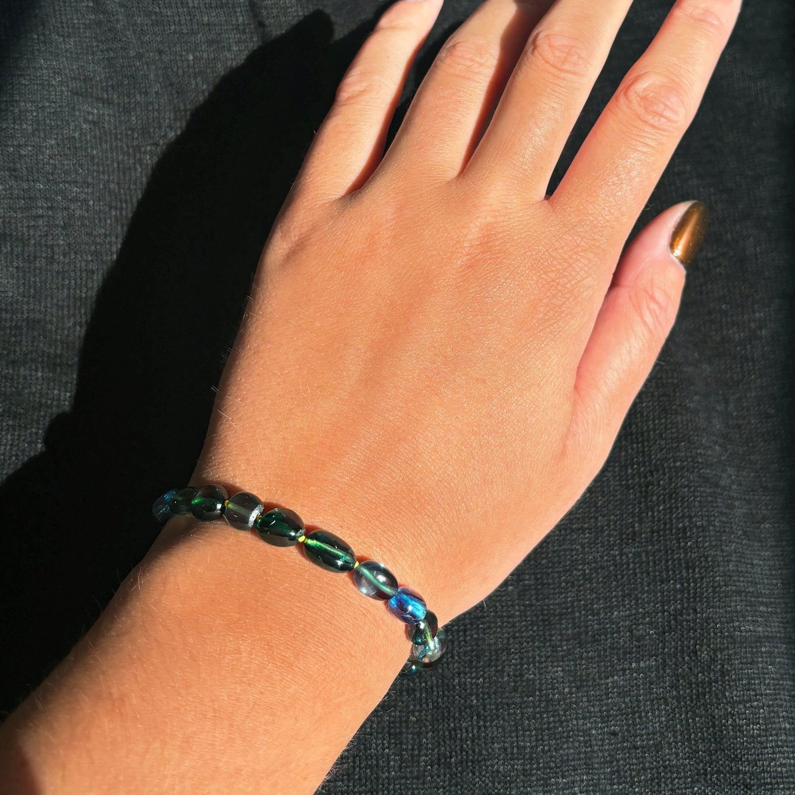 Shimmering beaded Green-Blue Spinel nugget bracelet with shades of green, blue, and team on a gold lobster clasp, on a wrist.