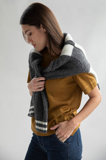 A model looking down wearing a gold sweater tee made from luxury alpaca silk, paired with dark blue denim jeans and a cozy grey plaid sweater wrapped around her shoulders.