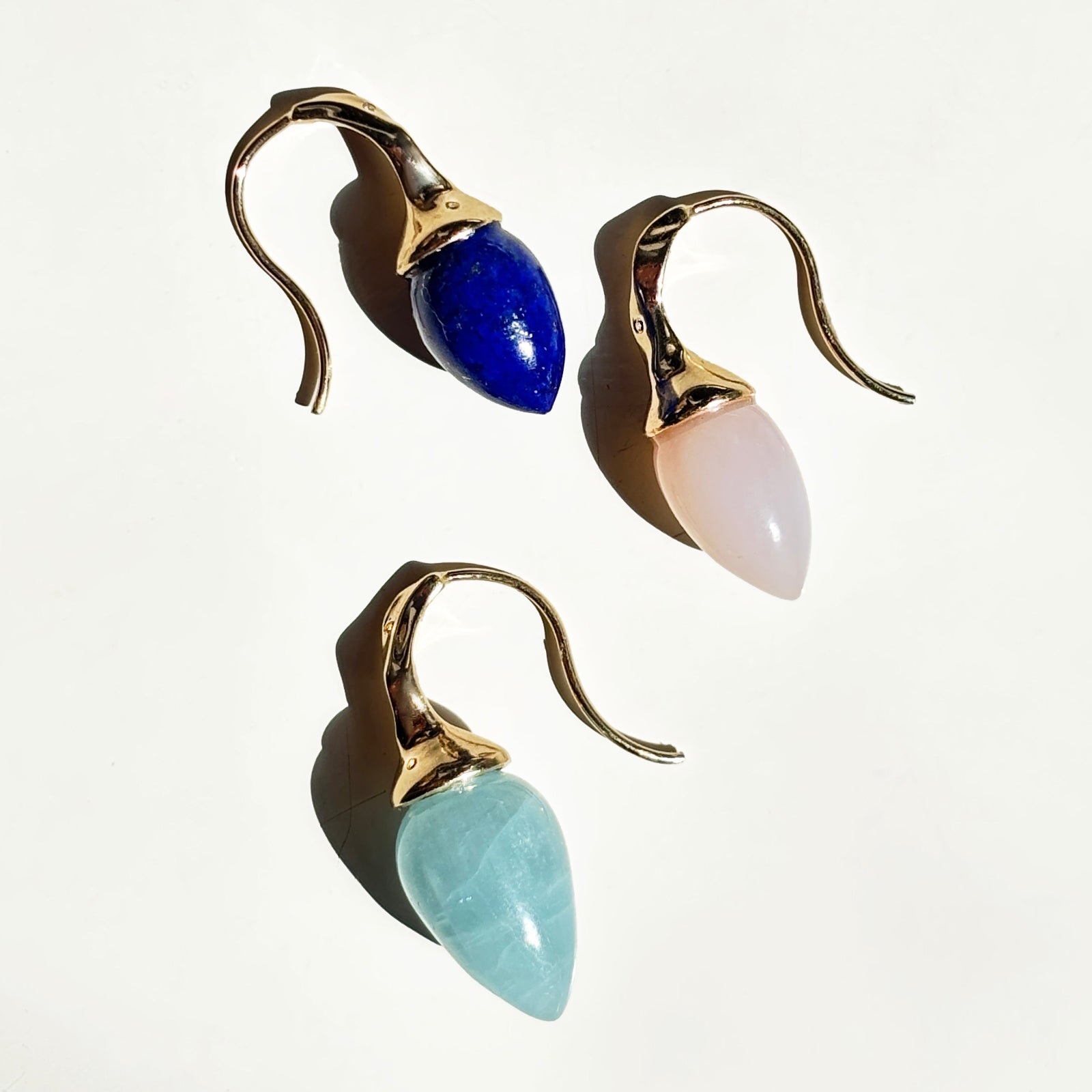Gemstone drop earring trio on white table in the sun.