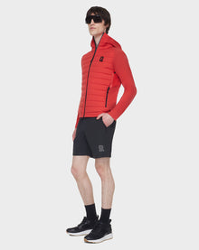 A man in dark sunglasses, black shorts, socks, and sneakers wears the RUDSAK JARRY - 6122007 POPPY RED RDS-certified down puffer jacket against a plain white background.