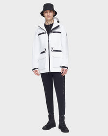 A person stands against a light gray background, wearing the RUDSAK JACY - 6122000 WHITE mid-length raincoat with black zippers, styled with a black bucket hat, pants, and boots.