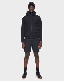 A man stands facing forward, wearing the RUDSAK JARRY - 6122007 BLACK puffer jacket with RDS-certified down, black shorts, athletic shoes, socks, and a cap—showcasing this cold-weather essential against a plain white background.