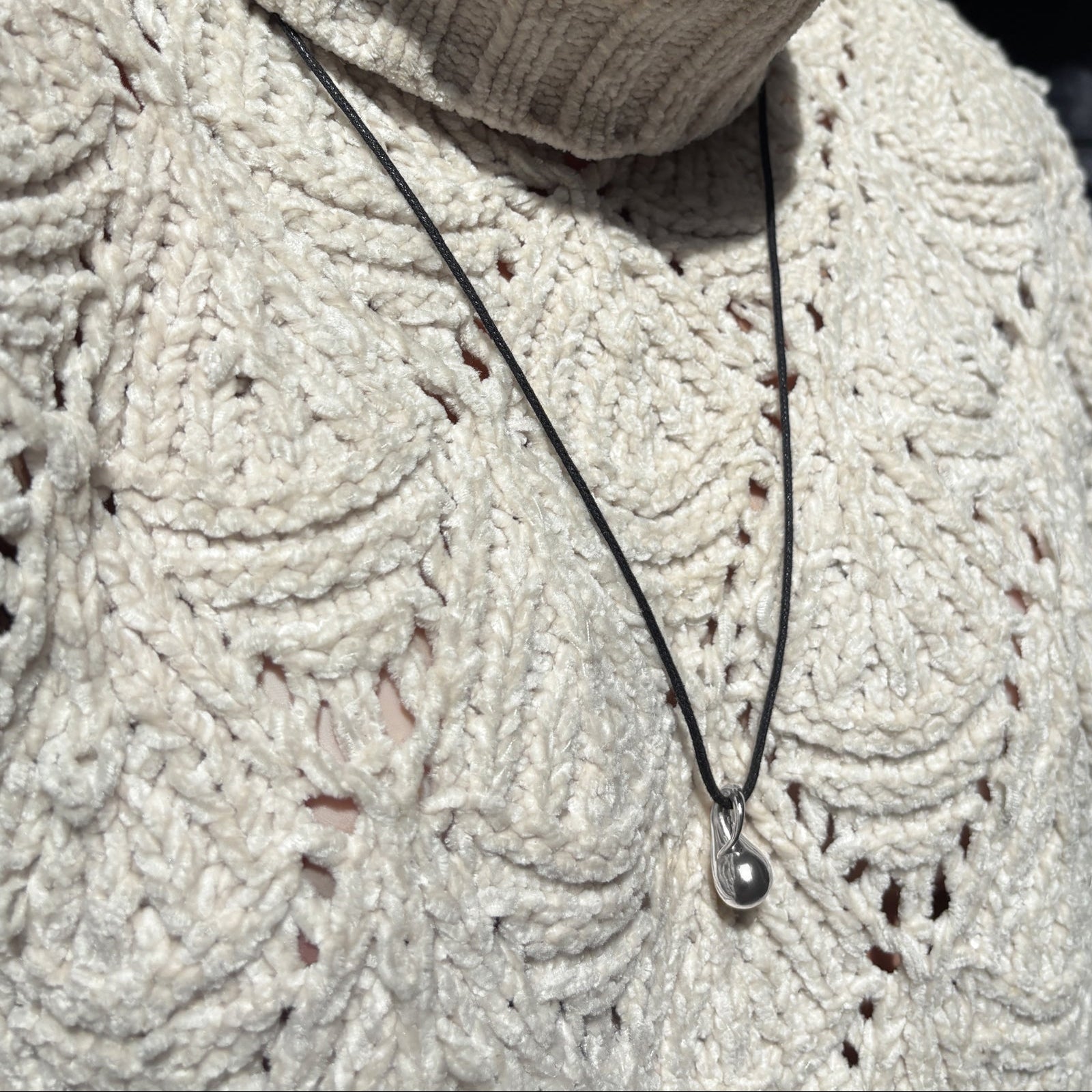 Molten Drop Charm in 14k white gold hanging from a quill cording over a cream sweater.