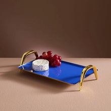 Blue tray with gold handles featuring a block of cheese and grapes on a brown background