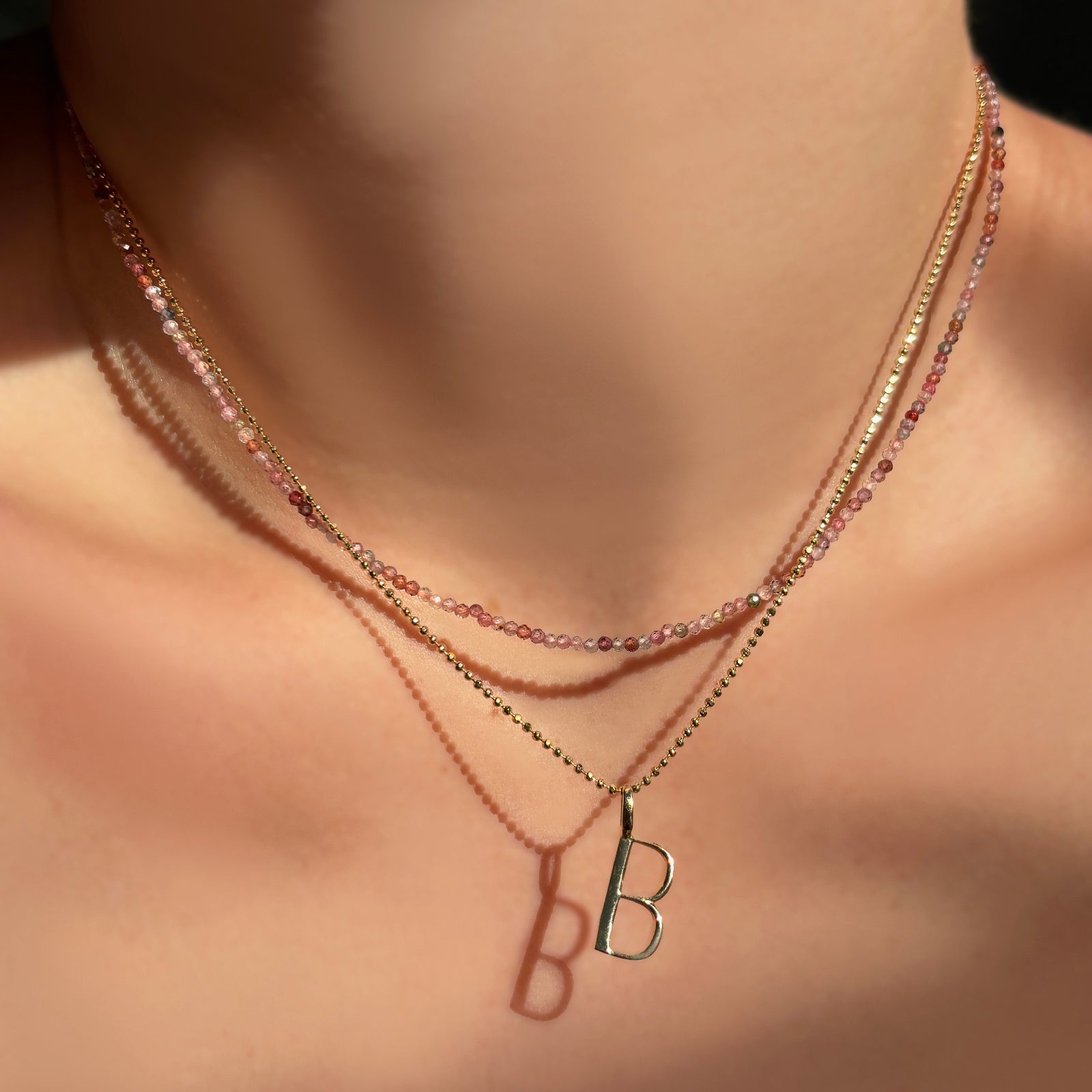 red pink faceted spinel layered with a diamond cut bead chain with a letter "B" charm on a model's neck.